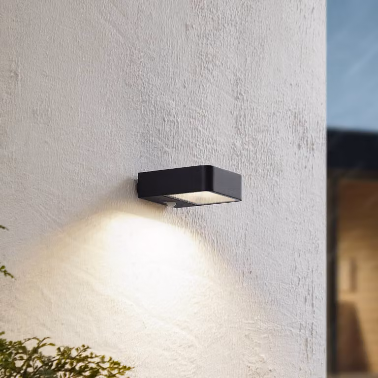 Lámpara solar LED de pared Lucande Dava en negro con sensor de movimiento y acabado en aluminio y cristal para exterior