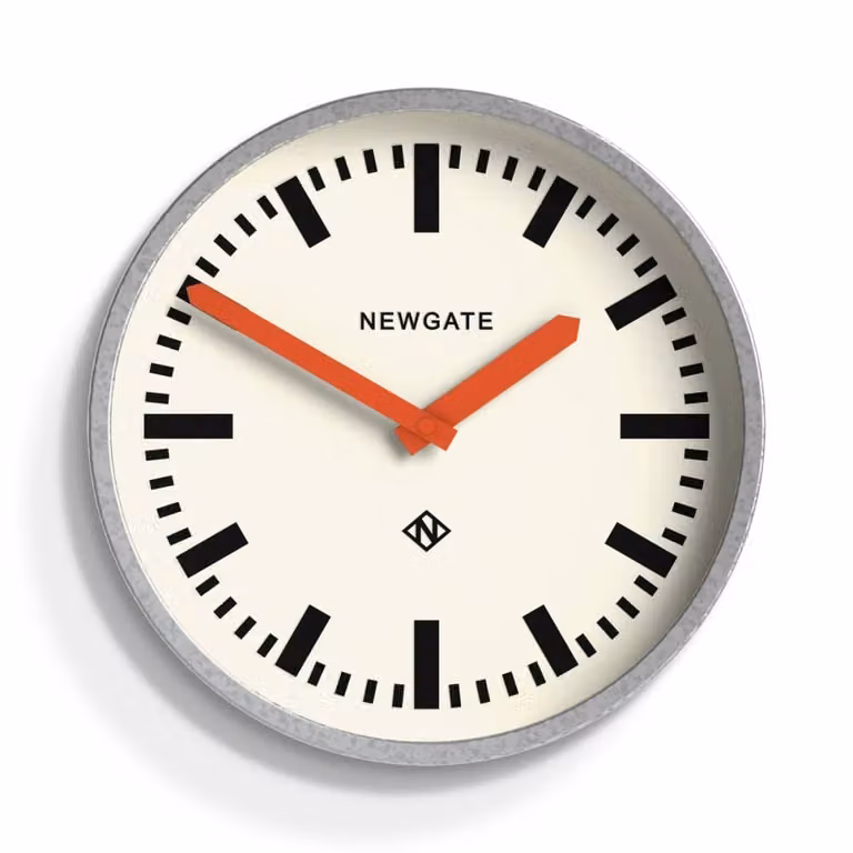 Reloj de pared analógico Newgate de estilo industrial con acabado metálico y agujas naranjas